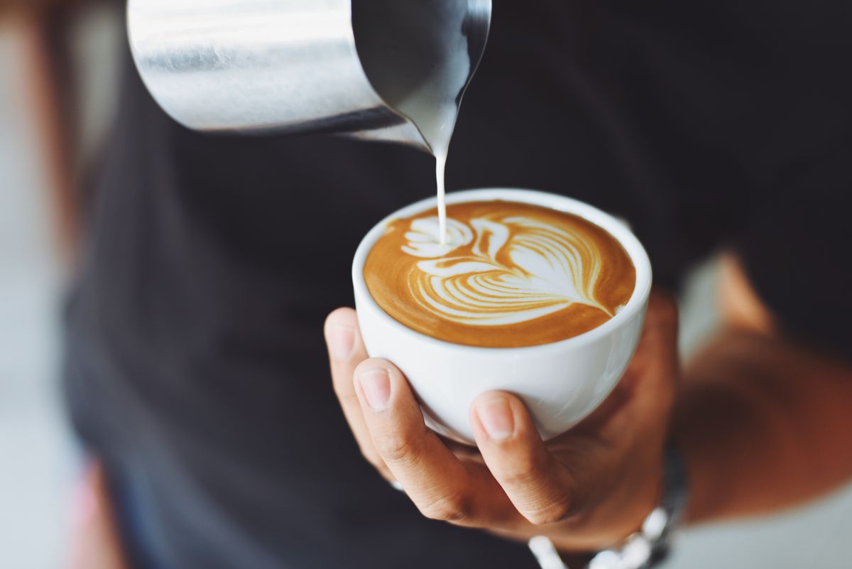 A barista pouring milk to finish a coffee