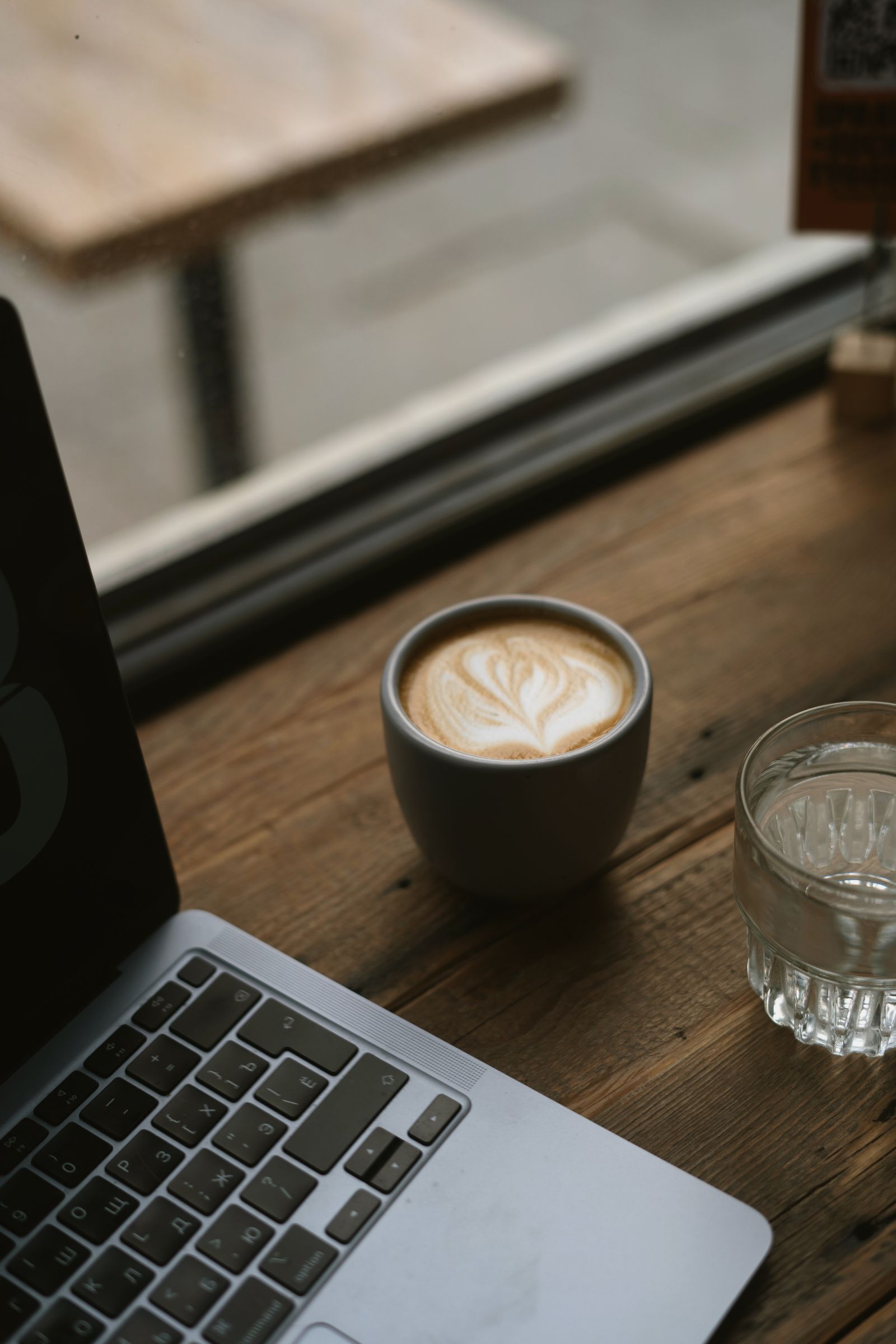 A laptop open beside a fresh latte on a café table