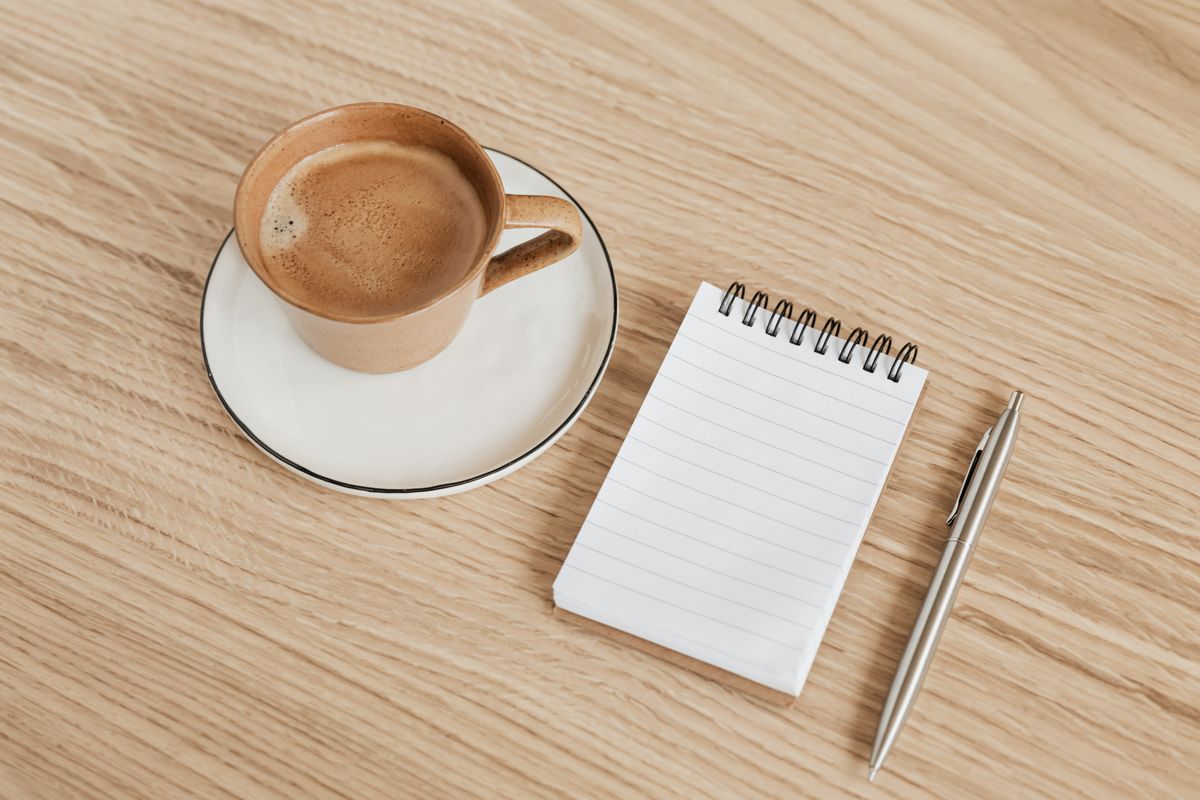 A coffee cup beside a notepad and pen on a desk